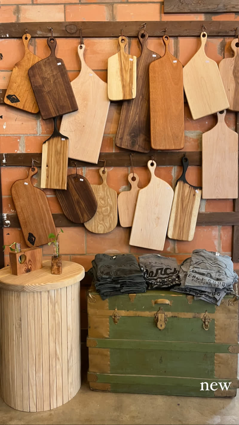 A wall of handmade cutting boards displayed above the green trunk in the Mercy Goods shop