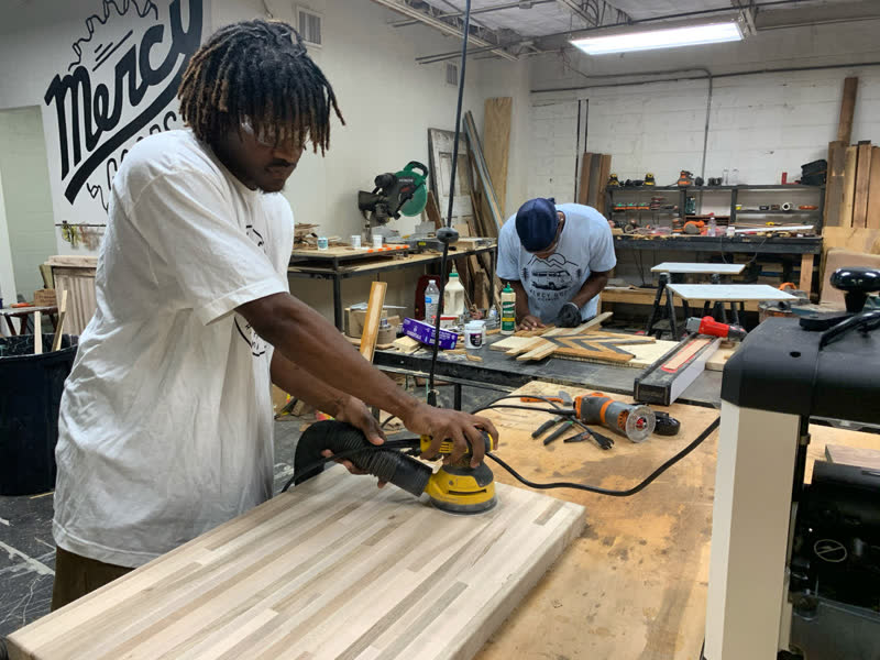 A student sanding a cabinet panel in the Mercy Goods workshop