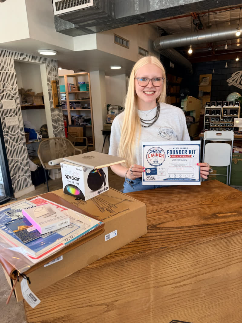A young woman holding her Mercy Launch Founder Kit certificate beside the kit box
