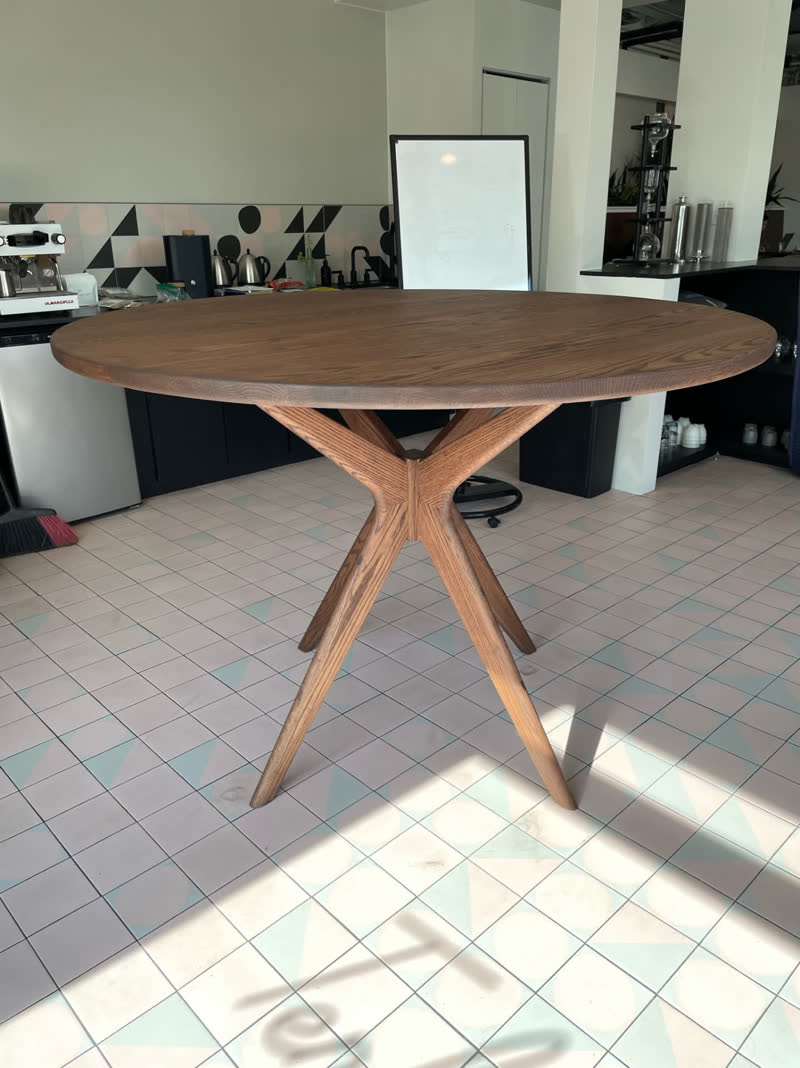 A round oak café table on a sculpted splayed-leg base