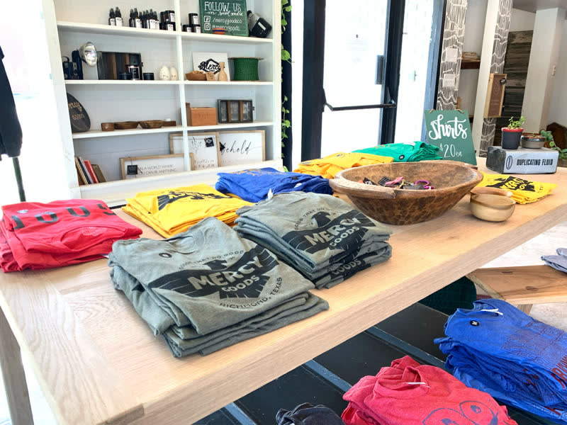 Mercy Goods t-shirts stacked on the shop's oak table, ready for customers