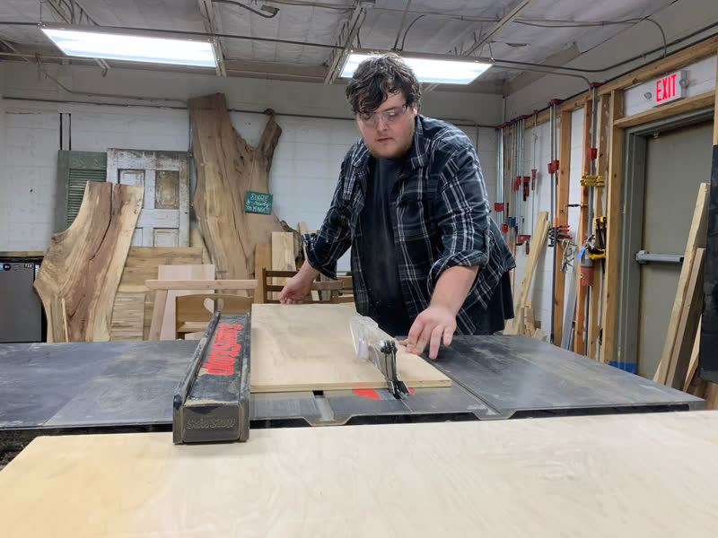 A young maker in safety glasses guiding a sheet through the SawStop table saw