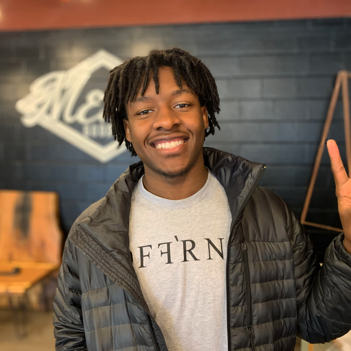 A smiling Mercy Goods participant flashing a peace sign in front of the Mercy Goods shop logo